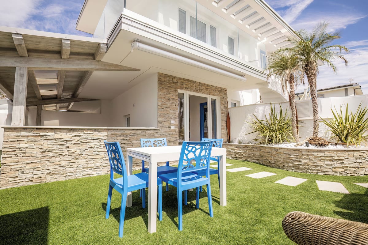 A modern house with a patio, stone wall, and a dining area with blue chairs.