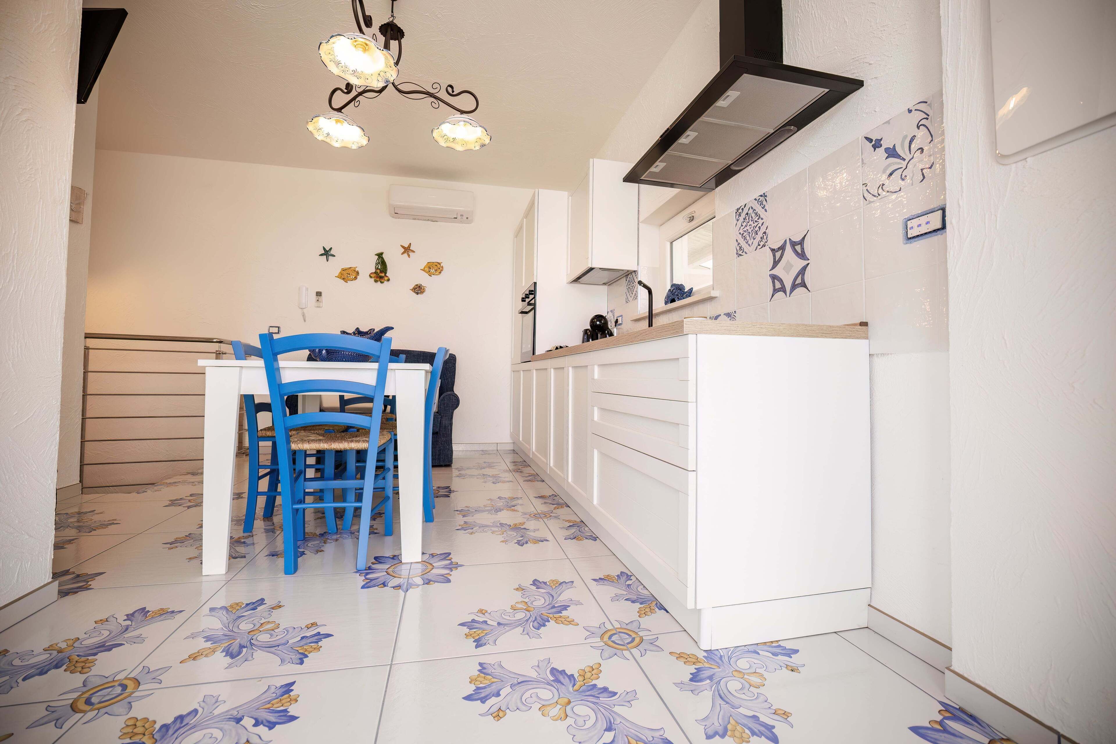 A kitchen with white cabinets, a blue chair, and a patterned tile floor.