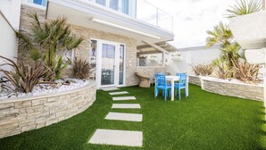A modern house with a stone exterior, a green lawn, and a patio with blue chairs. - Etoiles Guest House (Gioia Tauro)