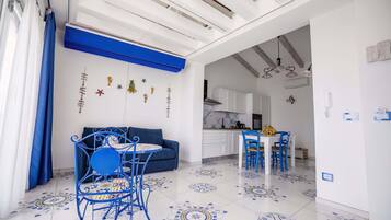 A modern living room with a blue sofa, a round table, and matching blue chairs. The room features white walls, blue accents, and patterned floor tiles.