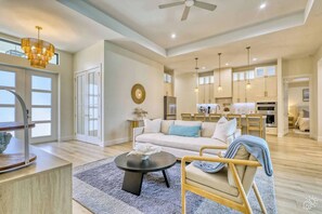 A spacious living area with a sofa, coffee table, and dining table. There is a kitchen in the background with modern appliances. - Stylish New Build with Pool, Spa, and Design (North Port)