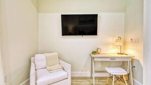 A room with a white sofa, a desk with a lamp, and a television on the wall. - Stylish New Build with Pool, Spa, and Design (North Port)