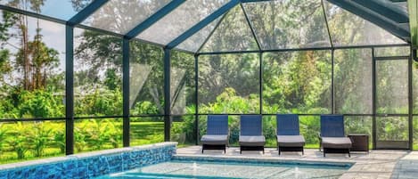 A covered outdoor swimming pool with lounge chairs and a view of greenery.