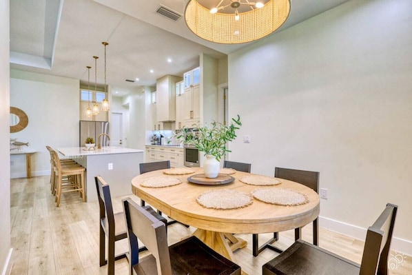 A modern dining area with a round wooden table, chairs, and a central plant. - Stylish New Build with Pool, Spa, and Design (North Port)