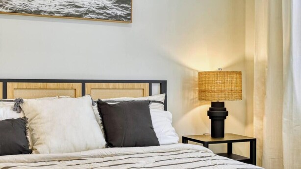 A bed with a headboard, pillows, and a bedside table with a lamp. - Stylish New Build with Pool, Spa, and Design (North Port)