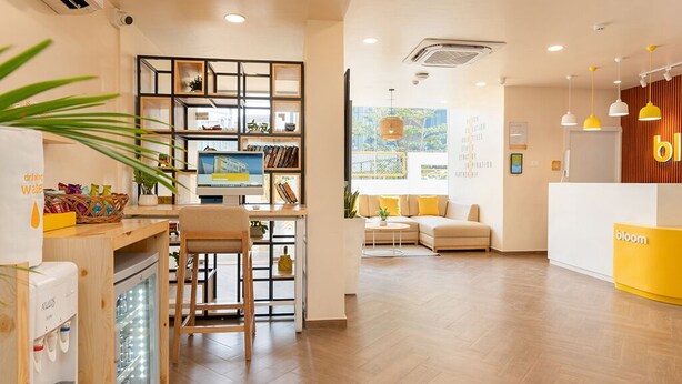 A modern hotel lobby with a reception desk, seating area, and a refreshment station. - Bloom Hotel Balewadi (Pune)