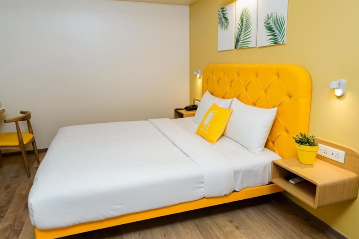 A bed with a yellow headboard, white bedding, and a small yellow plant on a bedside table.
