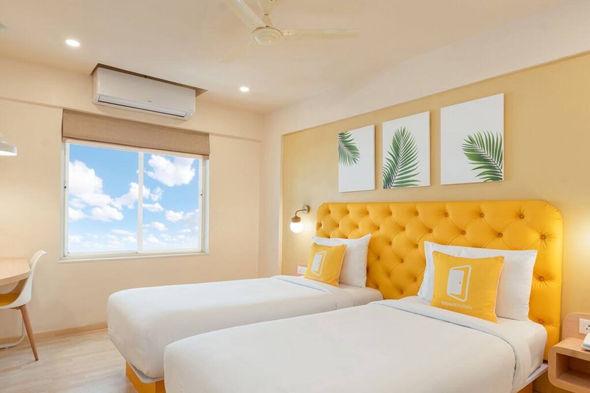 A hotel room with two beds, a desk, and a window with a view of the sky.