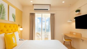 A hotel room with a bed, a desk, a chair, an air conditioner, a TV, and a window with curtains. - Bloom Hotel Balewadi (Pune)