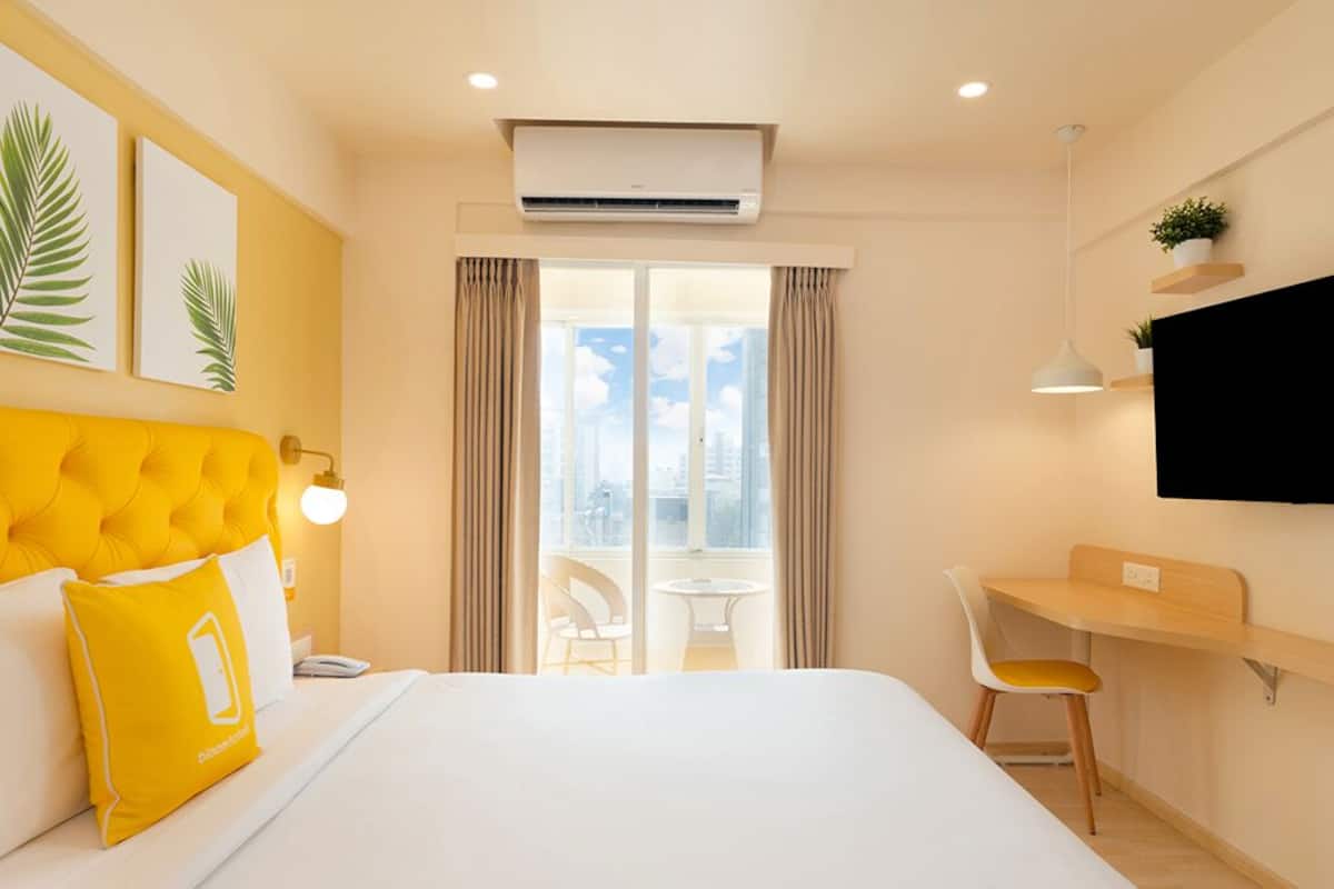 A hotel room with a bed, a desk, a chair, an air conditioner, a TV, and a window with curtains.