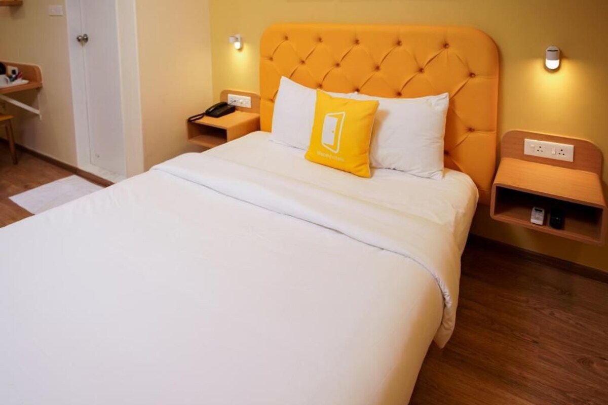 A hotel room with a large bed, a wooden nightstand, a bedside table, and a wall-mounted light.