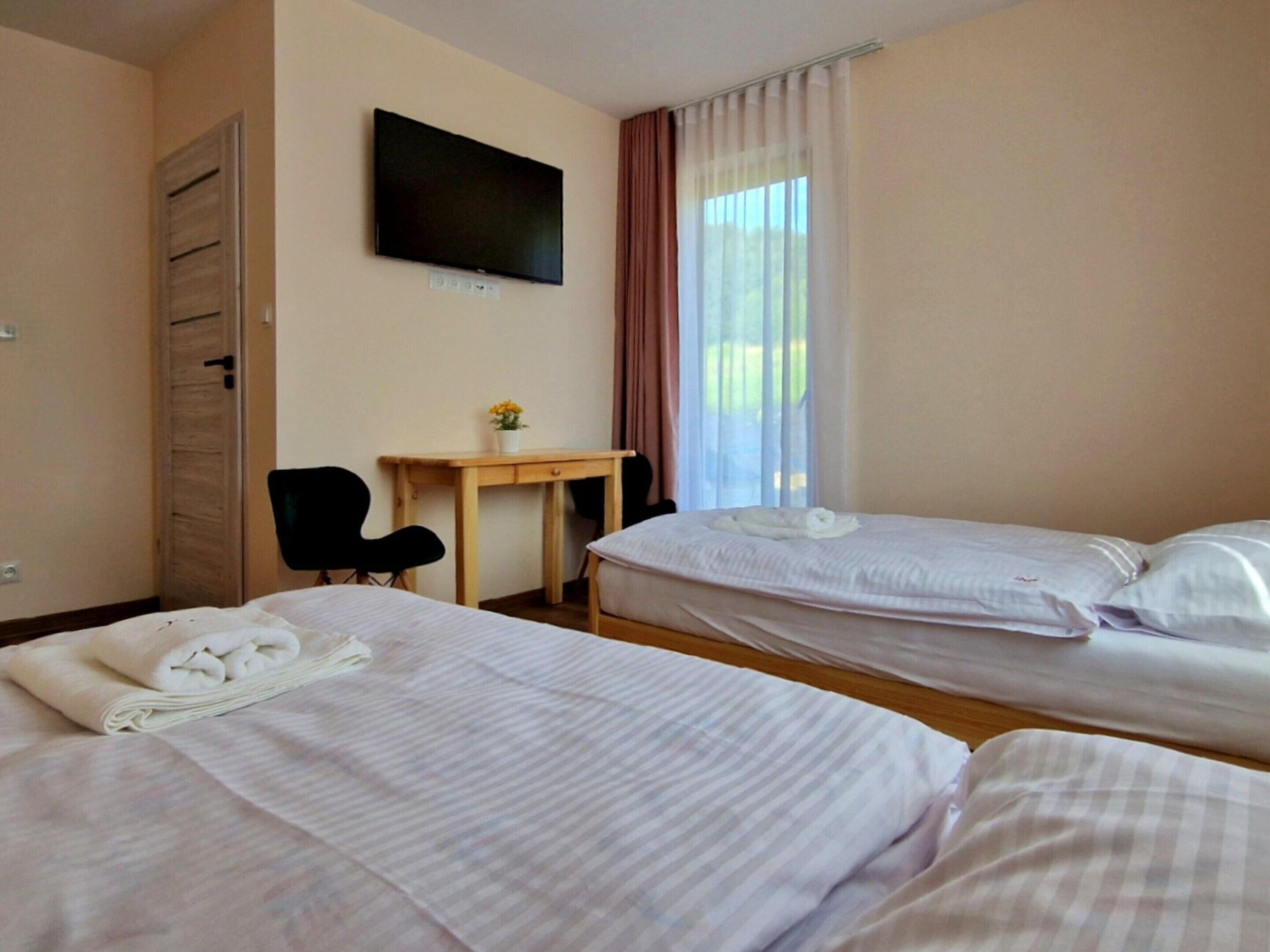 Habitación de hotel con dos camas, un escritorio, una silla, un televisor y una ventana con cortinas.