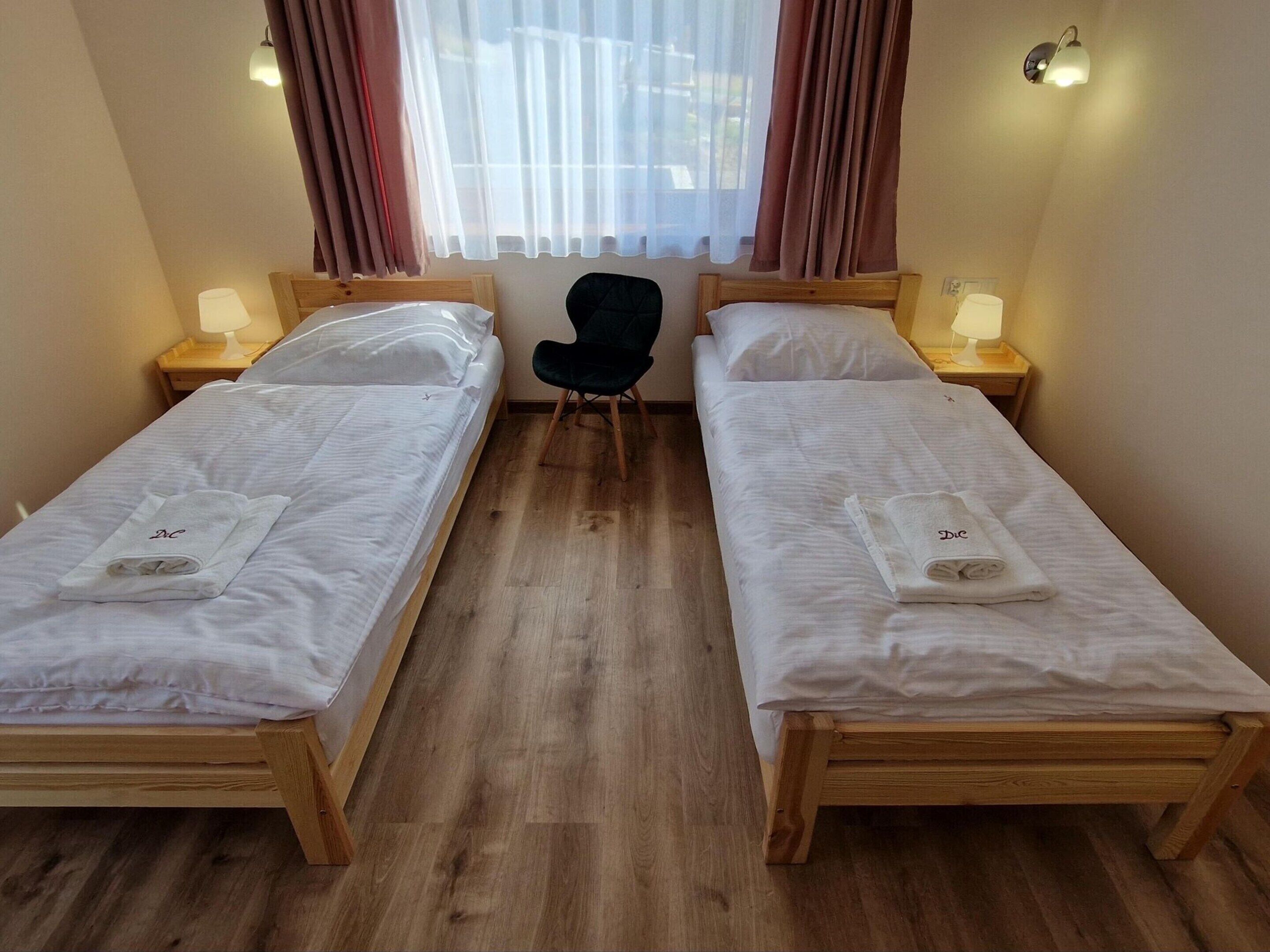 Habitación de hotel con dos camas individuales, una silla y un ventanal con cortinas.