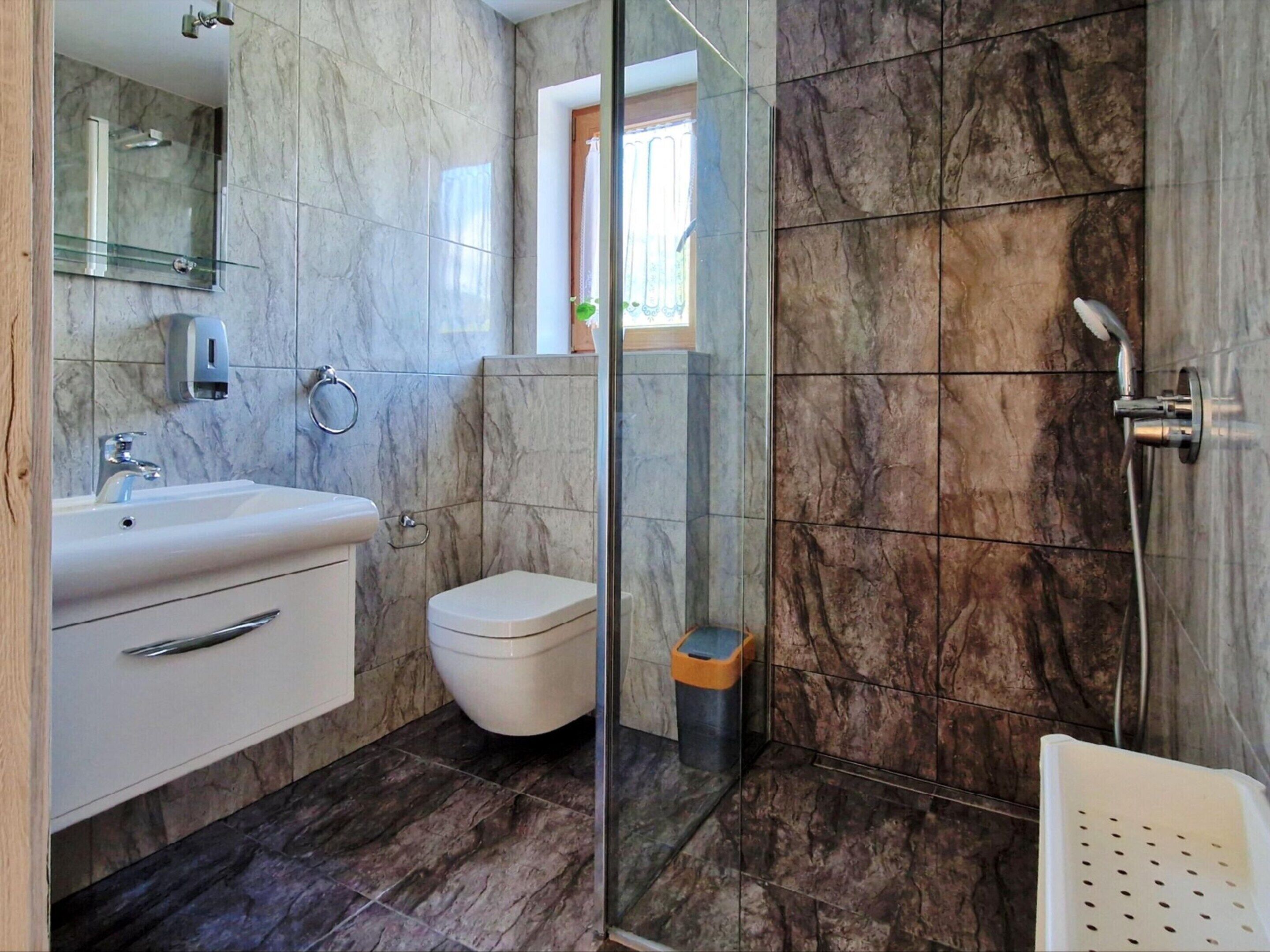 Un baño moderno con ducha de vidrio, lavabo con espejo e inodoro.
