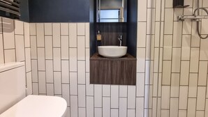 Une salle de bain avec des toilettes blanches, un lavabo avec un miroir au-dessus et une douche séparée par une porte en verre.