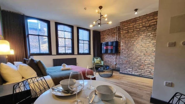 Un salon moderne avec un mur en briques, un téléviseur à écran plat et un coin repas avec une table mise pour deux personnes.