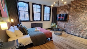 Une chambre d’hôtel moderne avec un grand lit, un téléviseur à écran plat, un mur en briques et une fenêtre avec des rideaux.