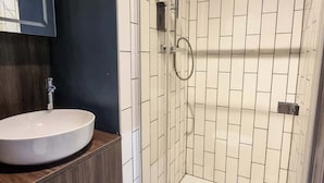 Une salle de bain moderne avec une douche à parois de verre, un lavabo rond et un meuble-lavabo en bois foncé.