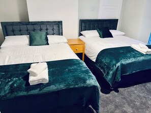 A hotel room with two beds, each with a dark green bedspread and white linens. There is a wooden nightstand between the beds. - The Coral Guest House  (Southampton)