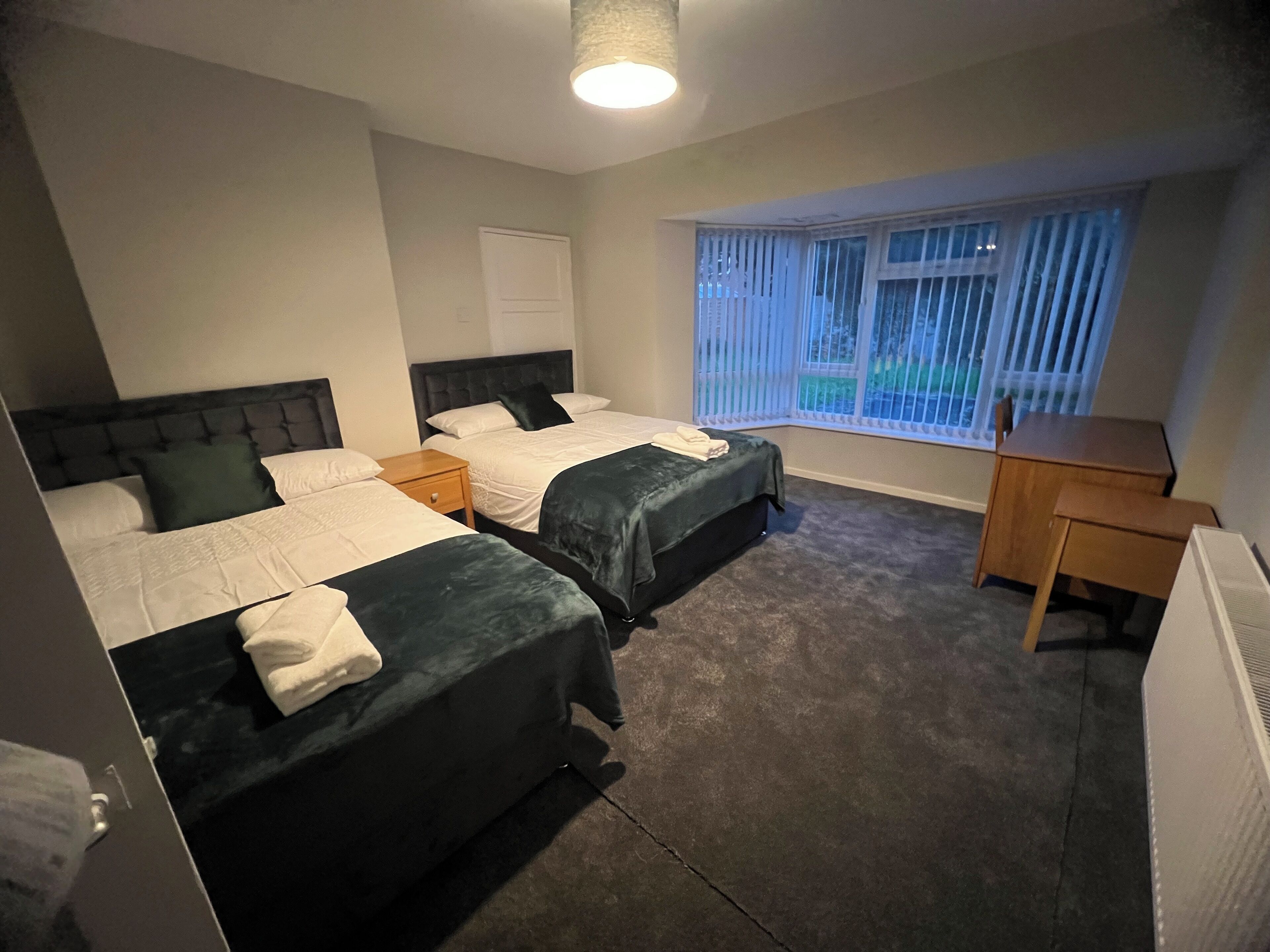 A hotel room with two beds, a desk, and a window with blinds.