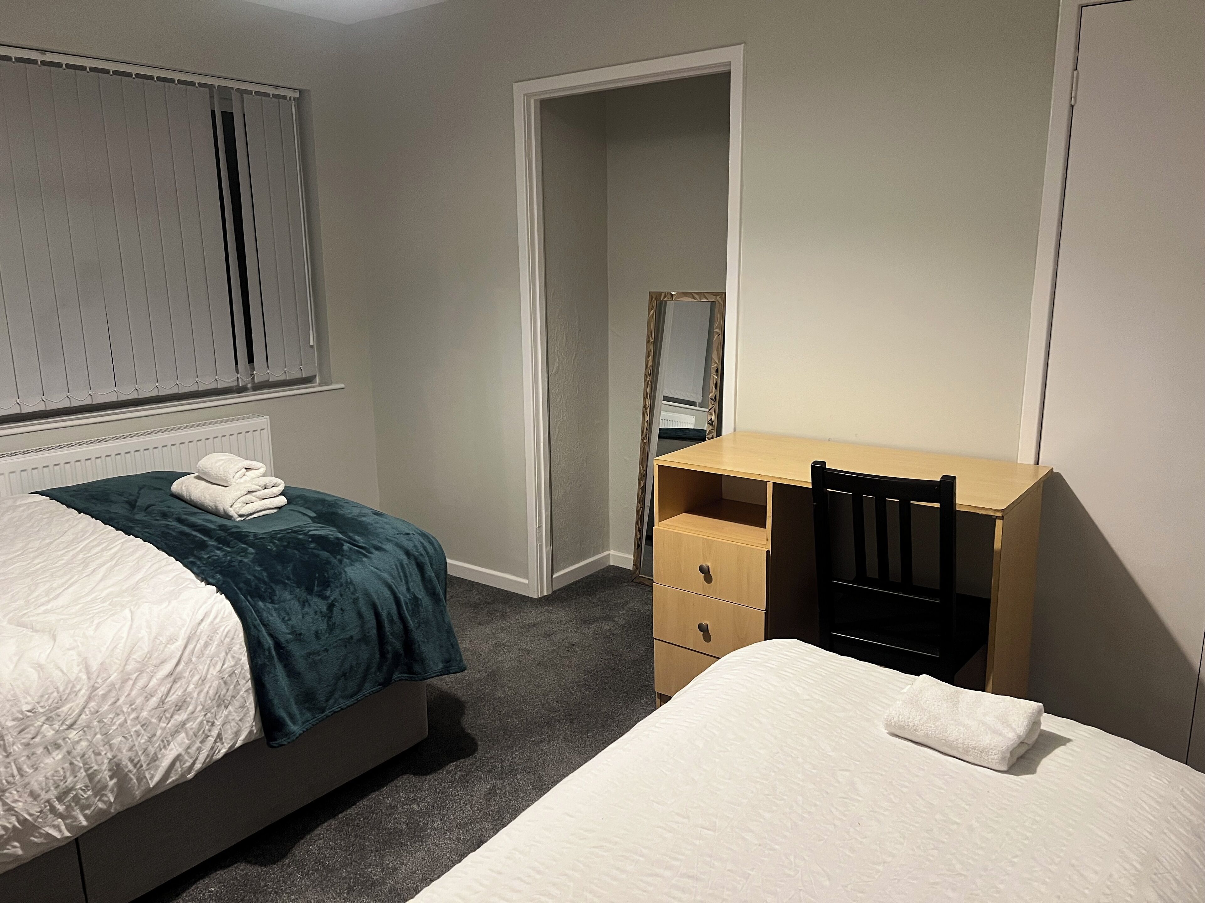 A bedroom with two beds, a wooden desk, a mirror, and a radiator.