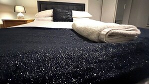 A neatly made bed with a dark blue bedspread and a folded white towel. - The Coral Guest House (Southampton)