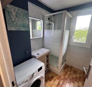 Ein kleines Badezimmer mit Waschmaschine, Waschbecken und Duschkabine.