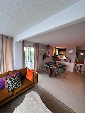 A modern living room with a sofa, a dining area, and a kitchen in the background.