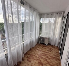 Un balcón con cortinas blancas, un aire acondicionado Toshiba y suelo de baldosas.