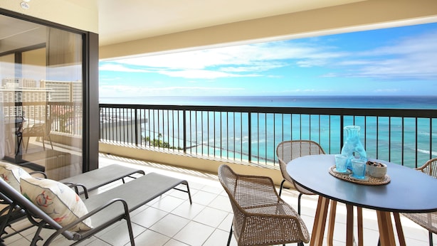 A balcony with a view of the ocean, wicker furniture, and a table with drinks.