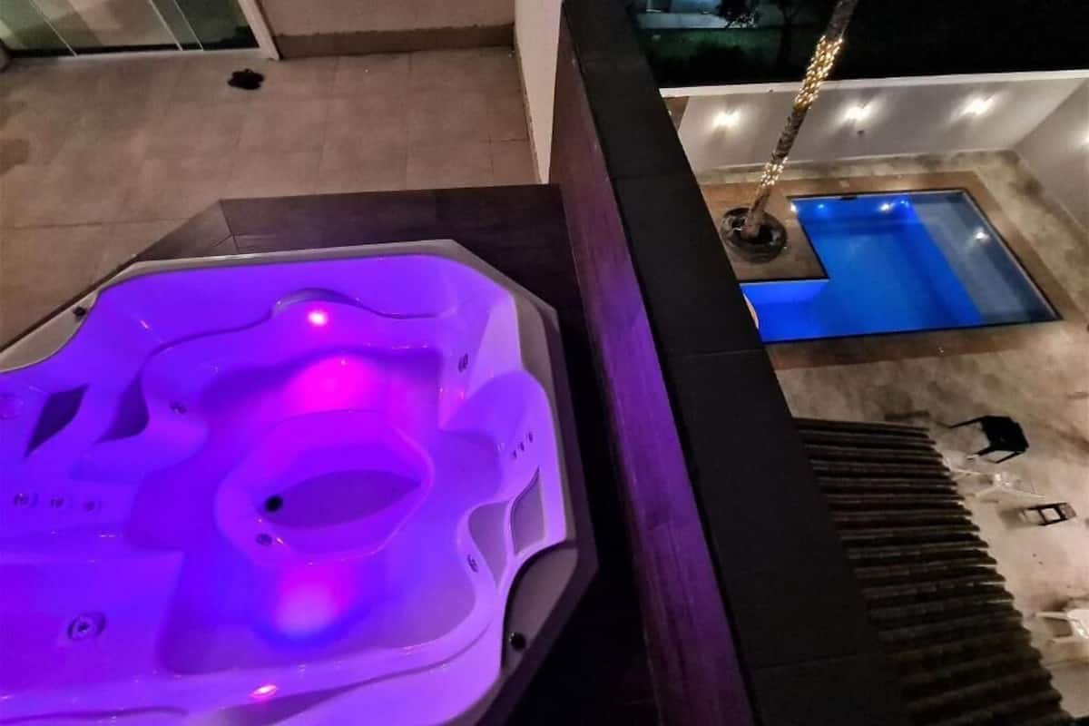 Egy jakuzzi, amelyen lila fény világít, egy kis medence, és egy lépcső, amely egy teraszhoz vezet.