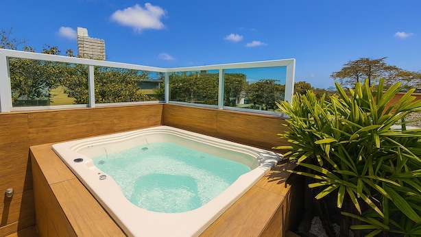 A hot tub with a wooden surround and glass panels, set against a clear blue sky. - Marmeu Enseada com jacuzzi aquecida (Guarujá)