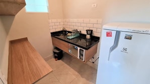 A compact kitchen with a black countertop, white tiles, a white refrigerator, and a small window. - Marmeu Enseada com jacuzzi aquecida (Guarujá)