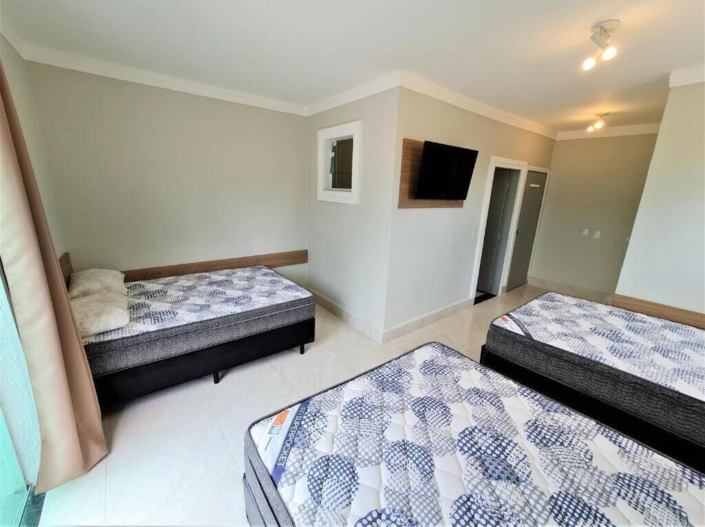 Ein Schlafzimmer mit zwei Betten, einem flachbildfernseher an der Wand und einer Tür zu einem weiteren Raum.