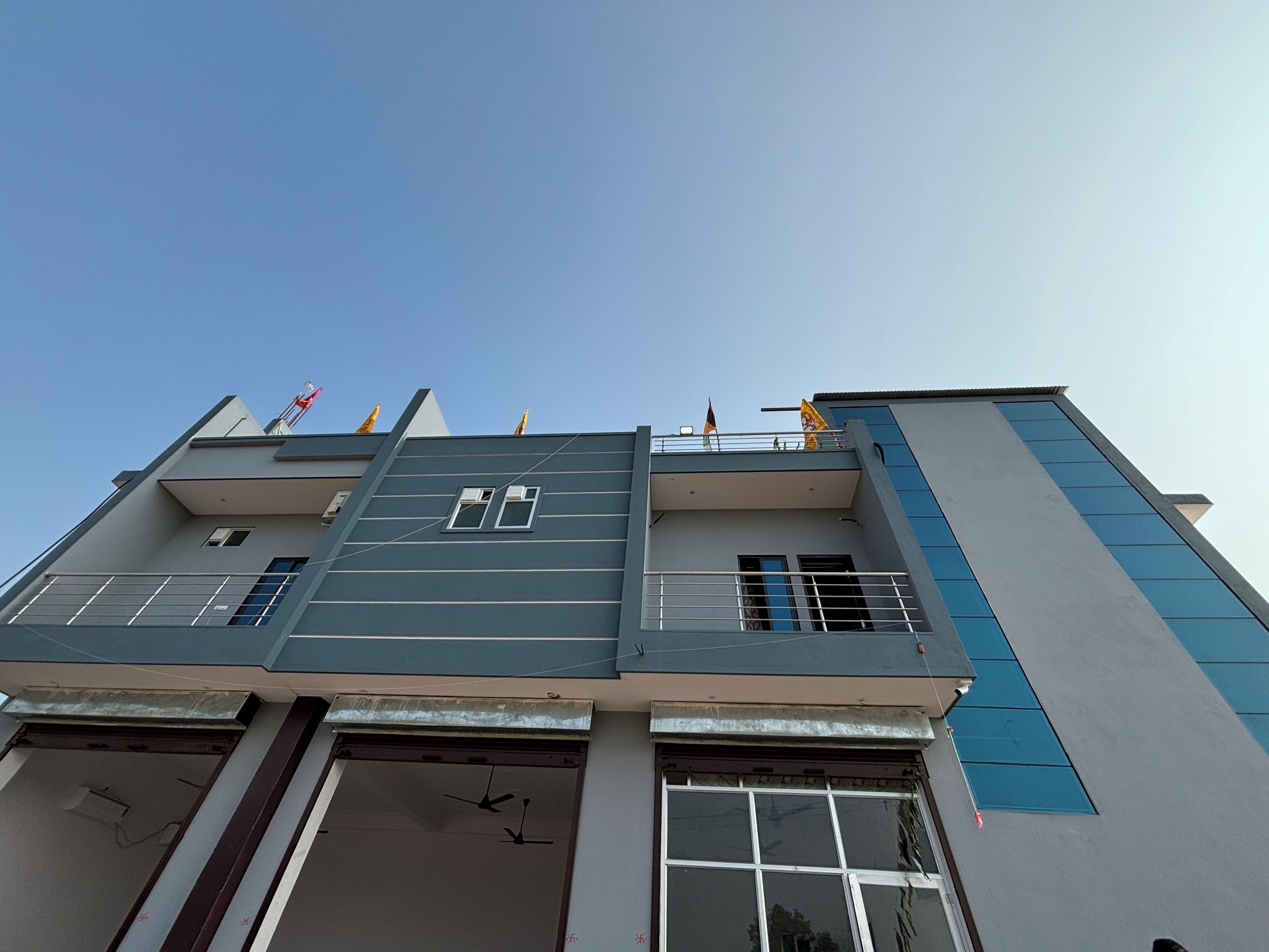 Un immeuble à plusieurs étages, doté d’un style architectural moderne, caractérisé par un toit plat, de grandes fenêtres et un balcon orné de drapeaux.