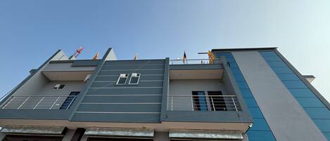 Un immeuble à plusieurs étages, doté d’un style architectural moderne, caractérisé par un toit plat, de grandes fenêtres et un balcon orné de drapeaux.