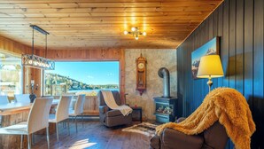 A wooden interior with a dining area, a fireplace, and a large window overlooking a scenic view. - Spa & Lake View | La Zenitude (Saint-Zénon)