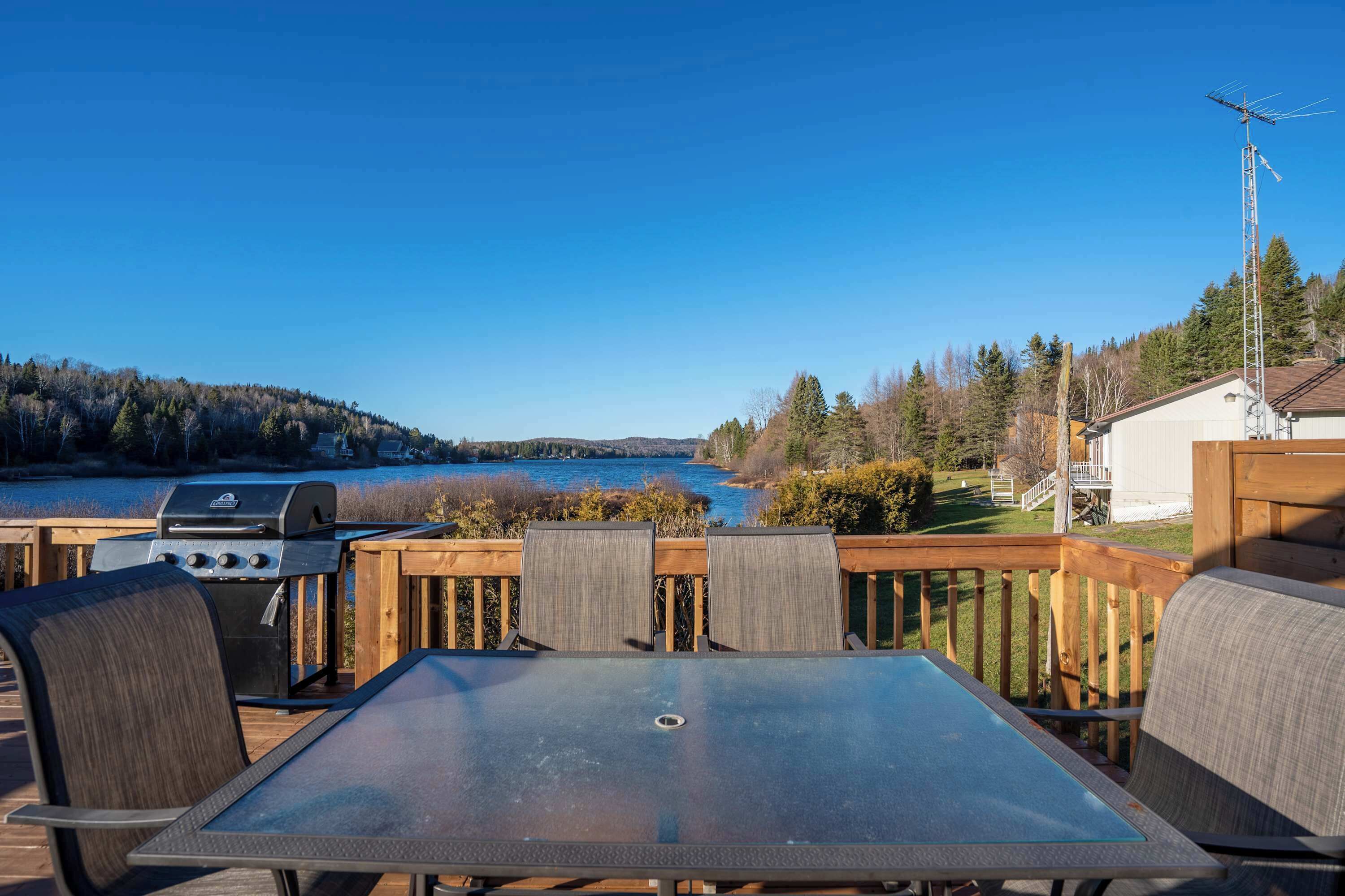Une terrasse extérieure avec une table et des chaises, offrant une vue sur un lac et des collines boisées.