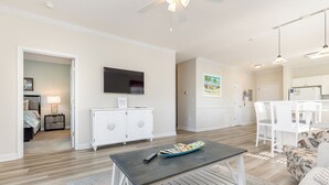 Una sala de estar moderna con televisor de pantalla plana, un comedor con sillas blancas y una cocina con gabinetes blancos.