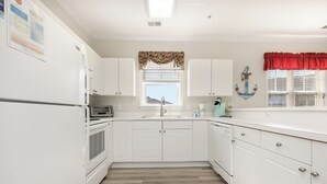 Una cocina con armarios blancos, un ventanal con un adornado floral y una cortina roja.