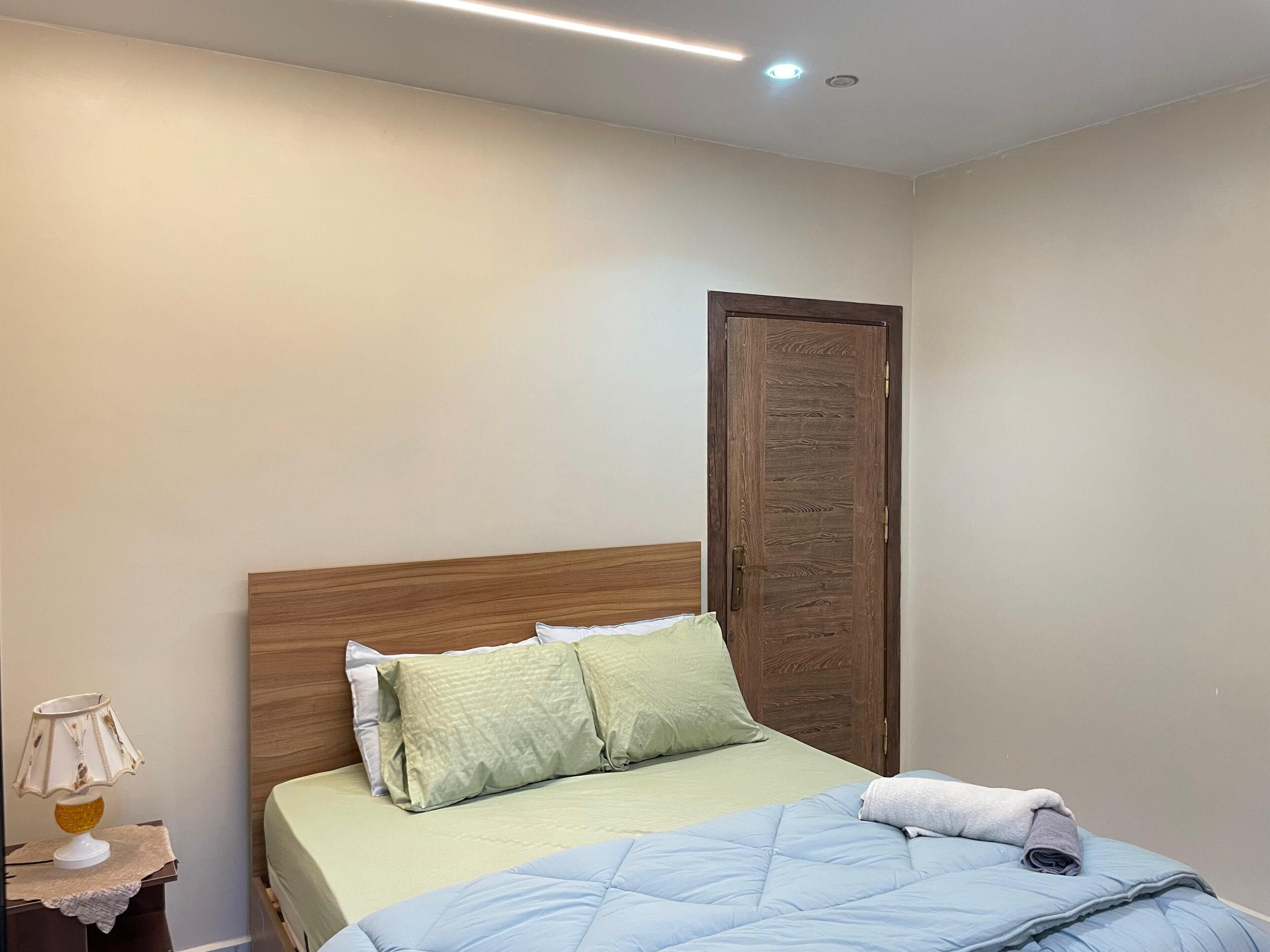 A bedroom with a bed, a wooden headboard, a nightstand with a lamp, and a door.