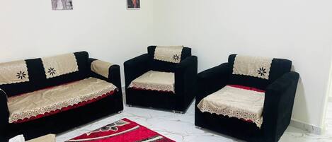 A living room with a black sofa set, a red patterned rug, and two framed pictures on the wall.