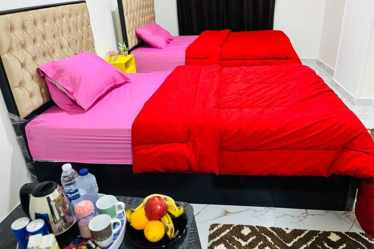 A hotel room with a bed, two pillows, a nightstand, and a tray with food and drinks.
