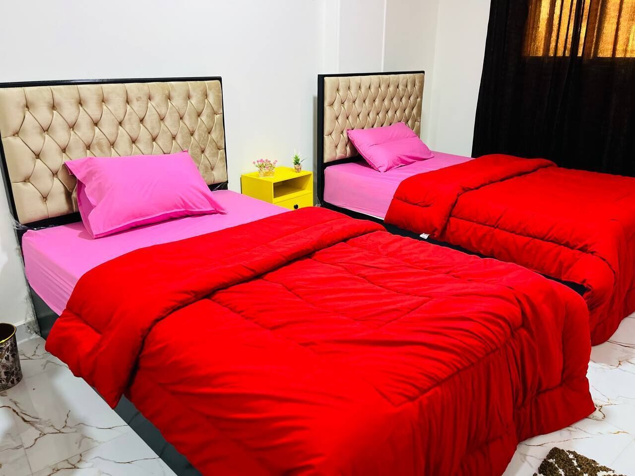 A hotel room with two beds, each with a tufted headboard and pink bedding.