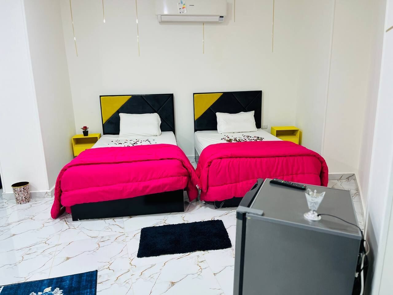 A hotel room with two beds, each with a black and yellow headboard, and a small desk with a TV and a glass.