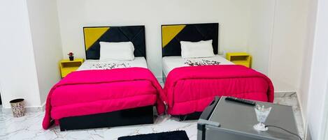 A hotel room with two beds, each with a black and yellow headboard, and a small desk with a TV and a glass.