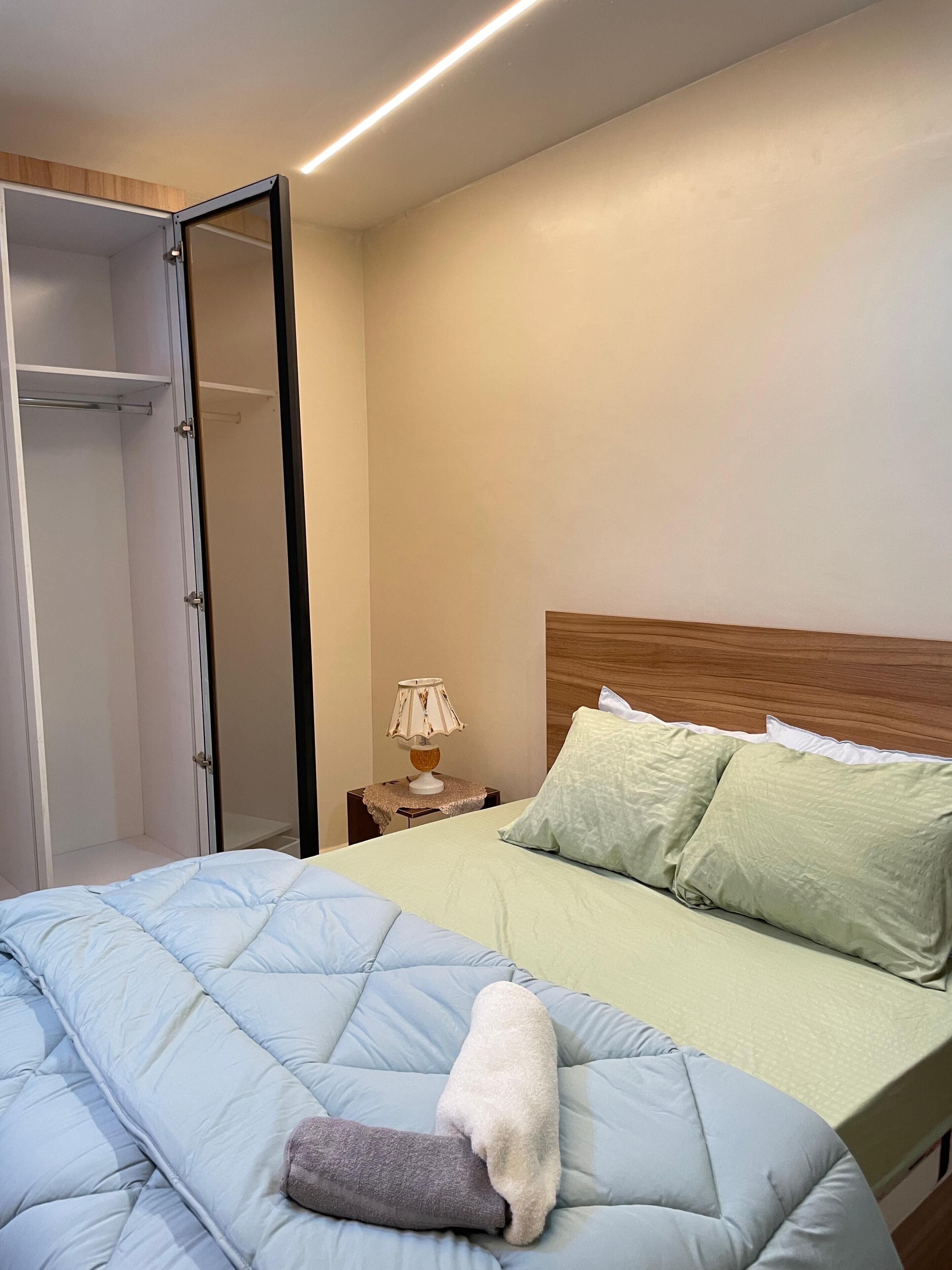 A bedroom with a bed, a nightstand with a lamp, and a wardrobe.