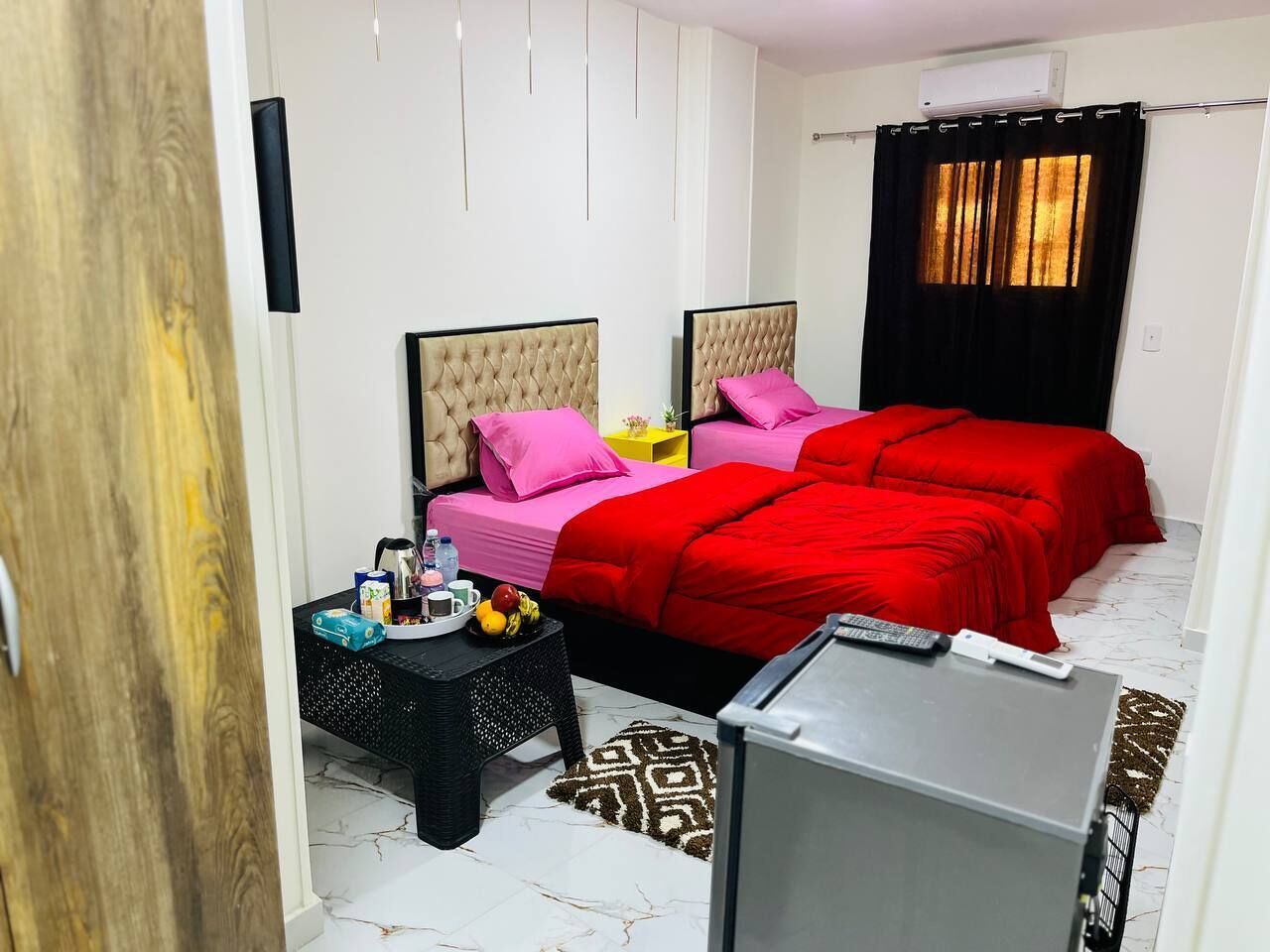 Un dormitorio con dos camas, una mesita pequeña, un televisor y una ventana con cortinas.