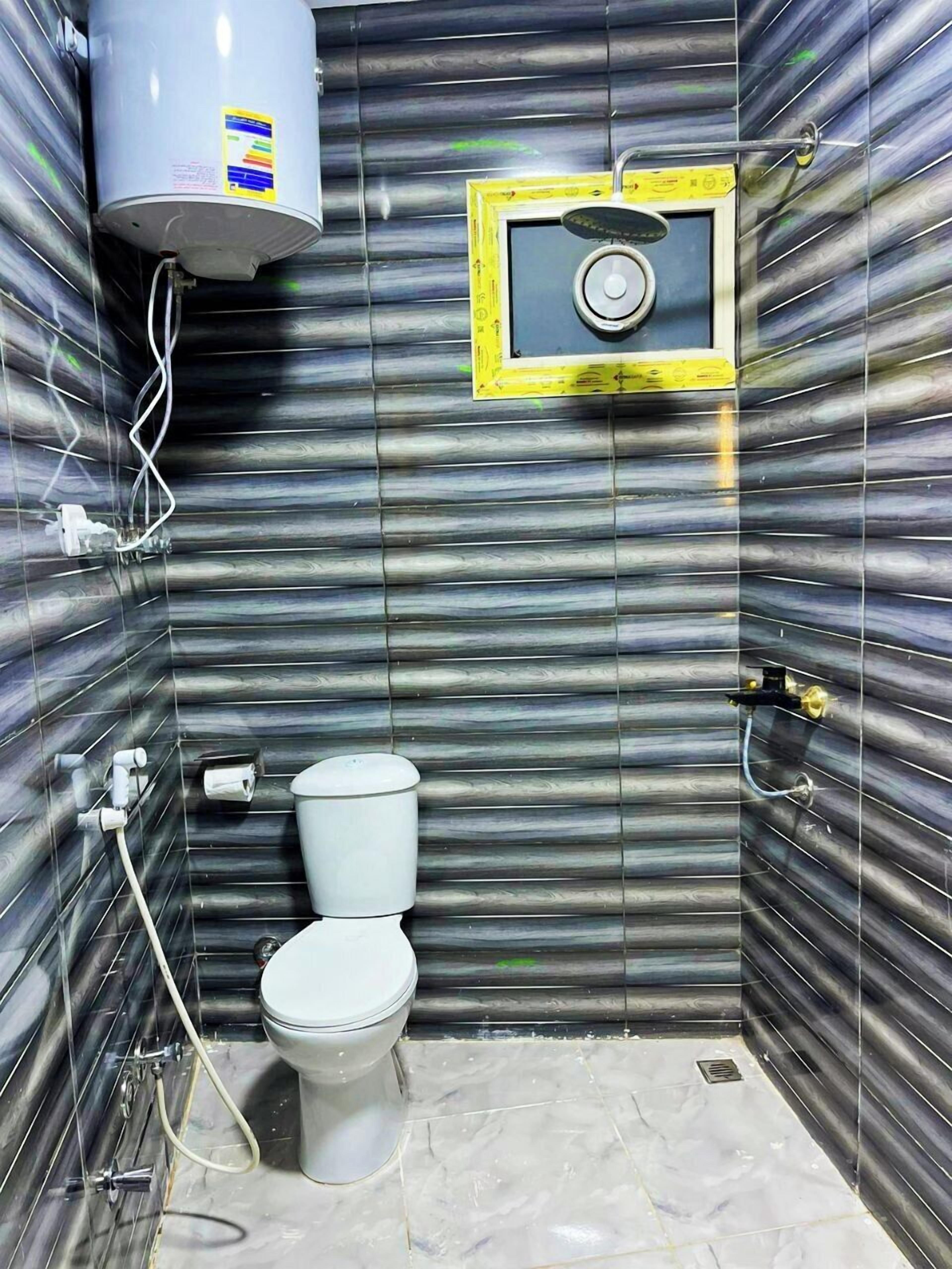 A bathroom with a toilet, a shower, and a water heater on the wall.