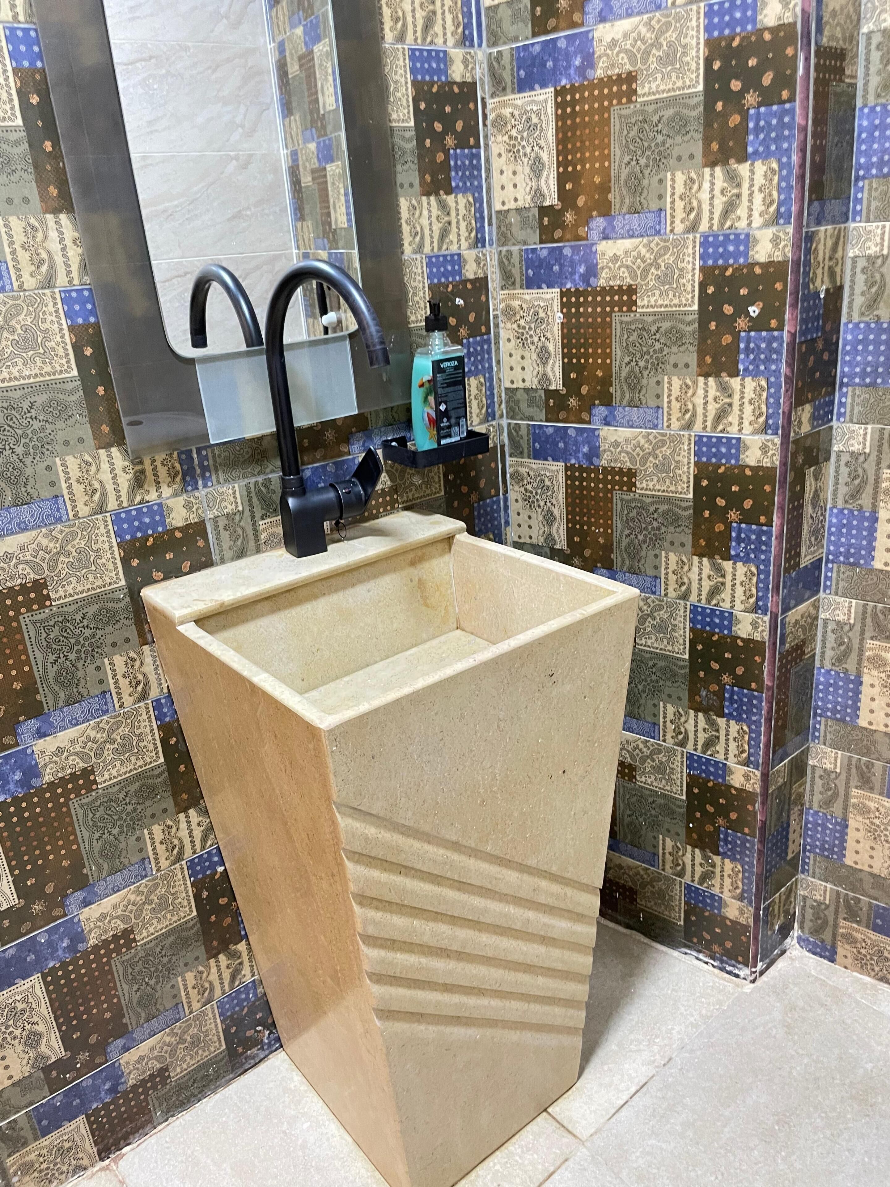 A bathroom with a sink, a mirror, and a patterned tile backsplash.